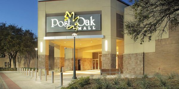 The Arbors at Wolf Pen Creek apartments Entrance of Post Oak Mall at dusk, with lit signage and surrounding plants.